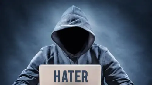 Hooded figure behind laptop labeled 'HATER'