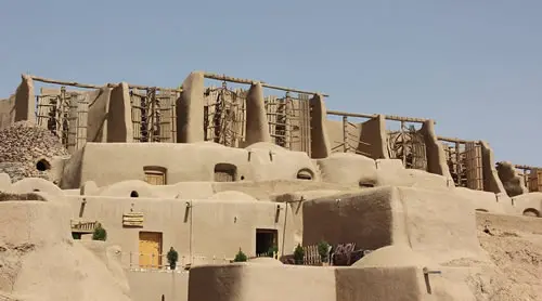 Ancient adobe structures with wooden beams in desert.