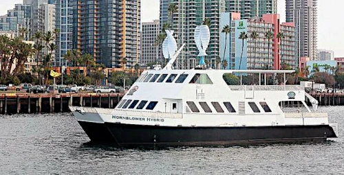 Hybrid ferry sailing near city skyline. With savonius wind turbine.