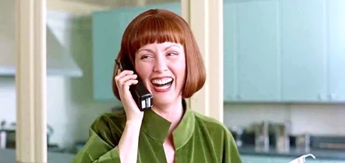 Woman laughing while talking on phone in kitchen.