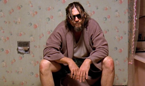 Bearded man in sunglasses and robe sitting on toilet.