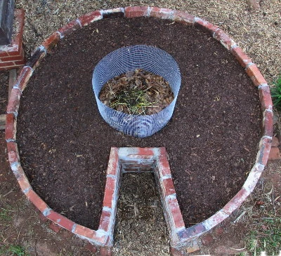 Huerto circular de ladrillo con cesta de compost en el centro.